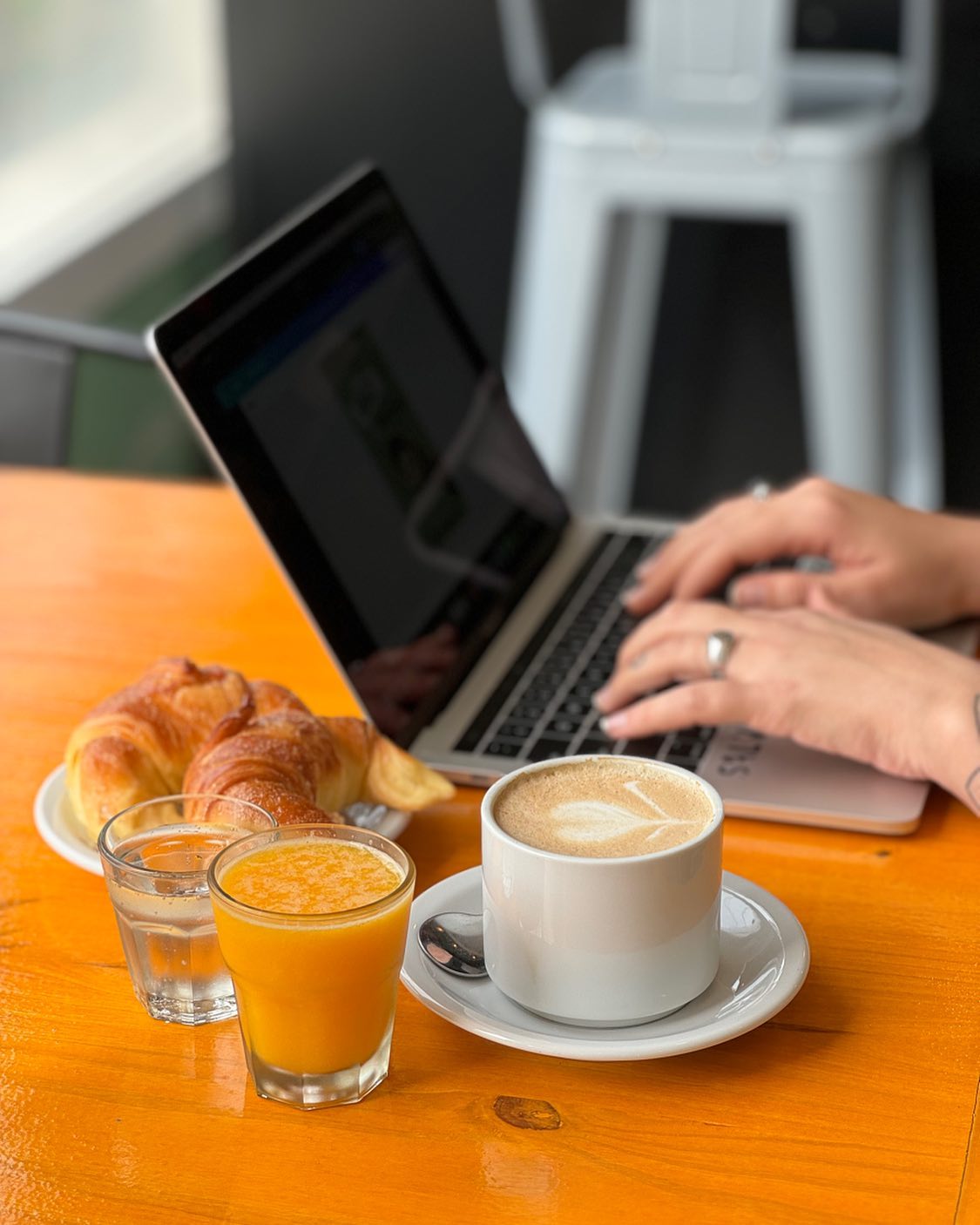 Mesa de coworking con laptop, café y medialunas en Salvatto
